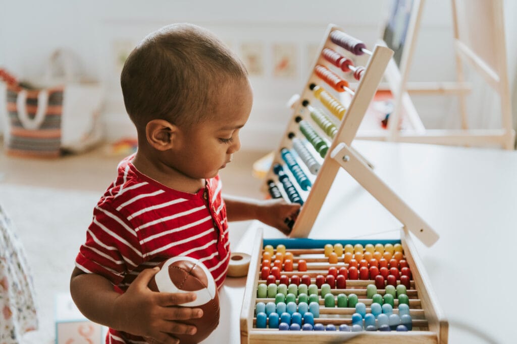 Toddler multi-tasking with a football and an abacus in their montessori nursery