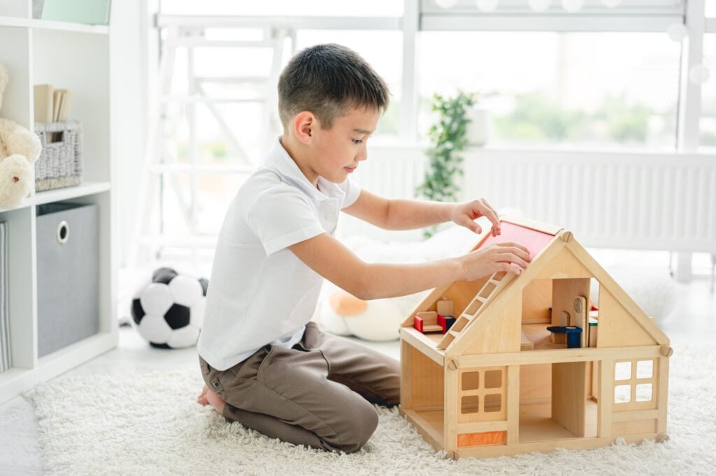 Boy playing with wooden Montessori dollhouse